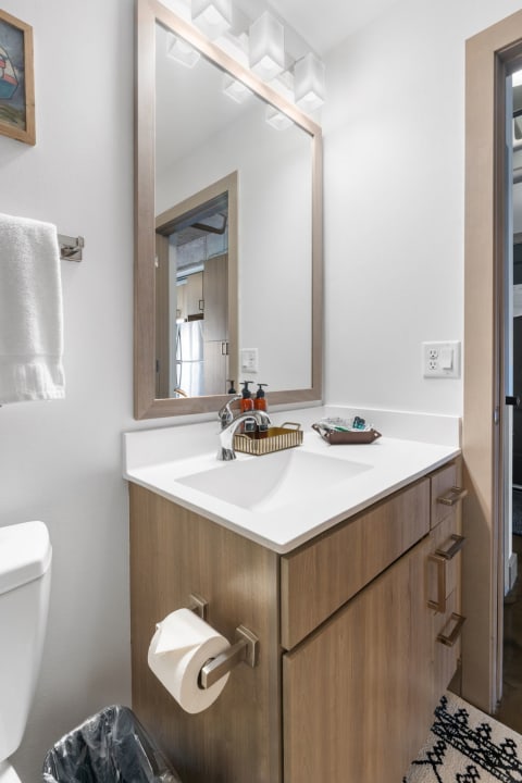 A modern bathroom featuring a stylish wooden vanity, mirror, and toiletries arranged on the countertop.