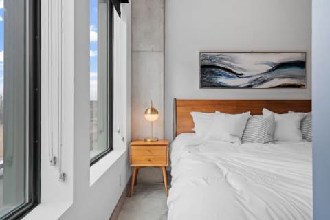 Modern bedroom with a wooden bed, decorative pillows, and contemporary artwork.