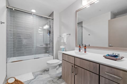Modern bathroom with a glass shower enclosure, white countertop, and soft wood cabinetry.