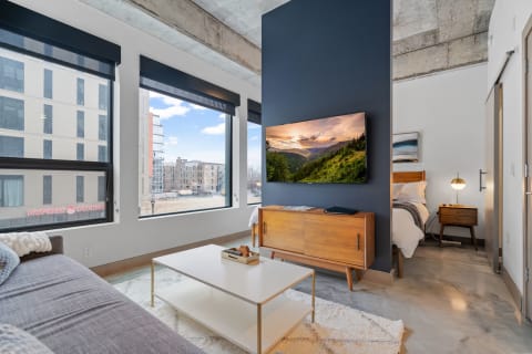 Interior view of a contemporary living area with a couch, large windows, and a scenic television display.