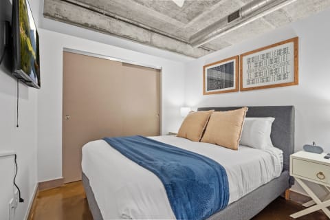 A cozy bedroom with a bed and modern decor, including a large TV and artwork.