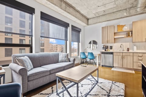 Interior view of a stylish living room with gray sofa, wooden coffee table, and modern kitchen.