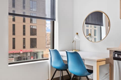 Modern workspace featuring a white desk, blue chairs, and a round gold-framed mirror by a large window.