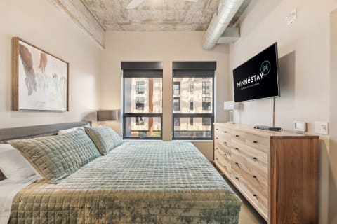 Modern bedroom with a king-sized bed, large windows, and a flat-screen TV.