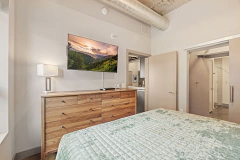 A modern bedroom featuring a mint green quilted bed and a mounted television displaying a landscape.