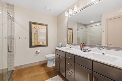 Modern bathroom with double sink vanity, framed artwork, and glass-enclosed shower.