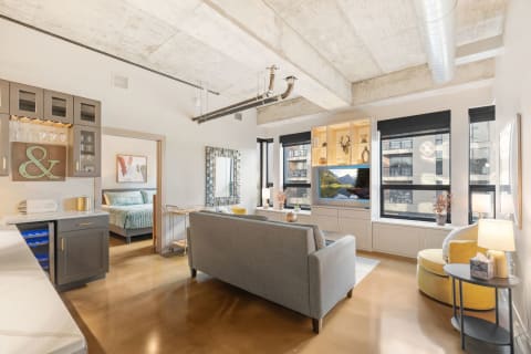 Modern studio apartment with gray sofa, yellow chair, and kitchenette.