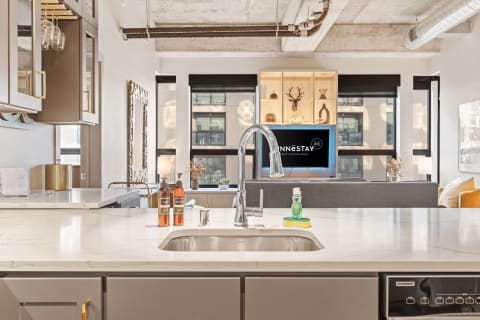 Contemporary kitchen with marble countertops and living space in the background.