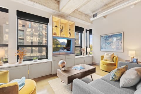 Modern living room featuring a gray sofa, yellow chairs, large windows, and an entertainment center with a TV displaying a nature scene.