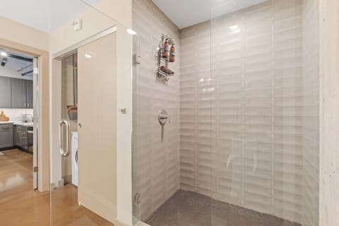 A contemporary shower with glass door, beige tiles, and hexagonal flooring.