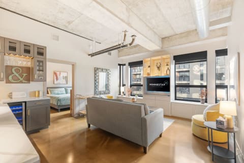 A contemporary living room featuring a gray sofa, yellow accent chair, and modern kitchen cabinetry.