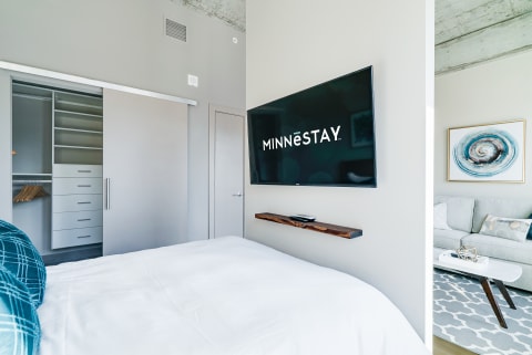 Modern bedroom interior showcasing a bed, mounted TV with MINNESTAY logo, and a closet.