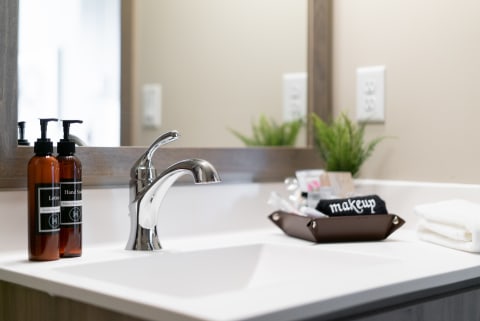 Modern bathroom countertop with a faucet, lotion and hand soap bottles, and a makeup tray.