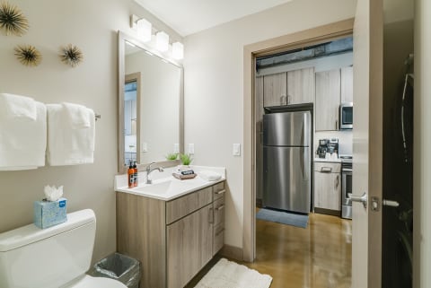 Contemporary bathroom featuring a vanity, mirror, and kitchen view.