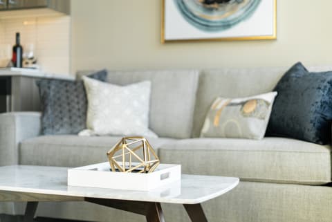 A contemporary living room with a marble coffee table, a geometric sculpture, and decorative pillows on a grey sofa.