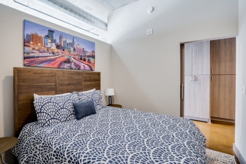 A contemporary bedroom with a patterned bedspread and a city skyline painting.