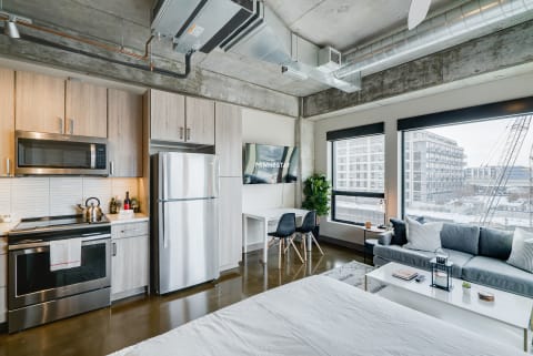 Modern studio apartment with kitchen, living area, and large windows providing natural light.