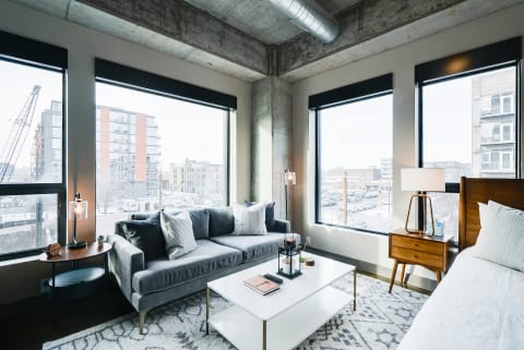 Spacious living room with large windows, gray sofa, and white coffee table in an urban setting.