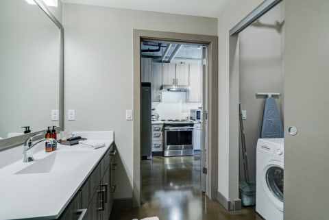 Interior view of a modern bathroom leading to a kitchen and laundry area.