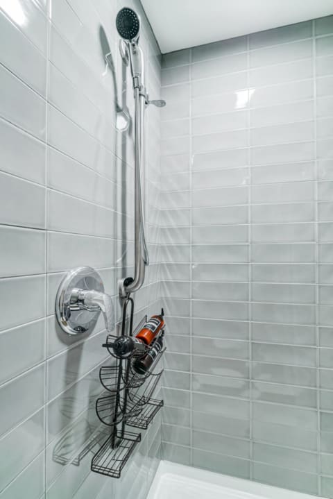 Shower space featuring gray tiles, silver showerhead, and black wire caddy with toiletries.