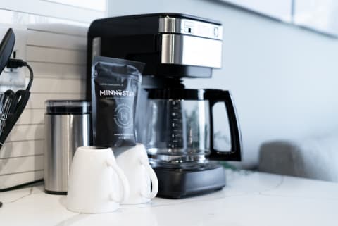 A sleek coffee maker with white mugs and a coffee packet on a kitchen countertop.