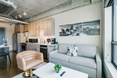 Modern apartment interior with a grey sofa, blush accent chair, and a kitchen.