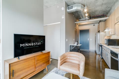 Interior view of a contemporary vacation rental with a lounge chair, television, and kitchen area.