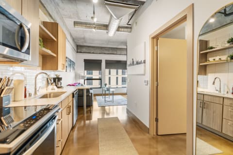 Modern kitchen with wooden cabinets and stainless steel appliances leading to a living area with a sofa and coffee table.
