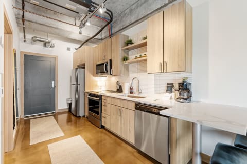 A contemporary kitchen featuring stainless steel appliances, light wooden cabinetry, and a marble countertop.
