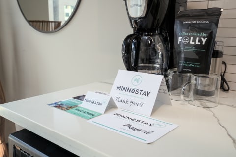 A countertop in a vacation rental featuring a coffee maker, informational cards about MINNéSTAY, and two glass cups.