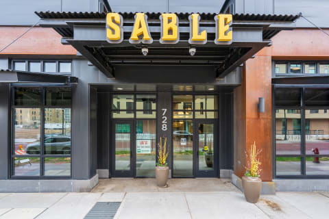 Entrance of a building named SABLE with glass doors and large windows, featuring a decorative planter.