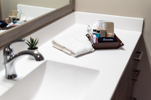 Modern bathroom countertop featuring a chrome faucet, towel, cosmetic tray with grooming items, and a small plant.