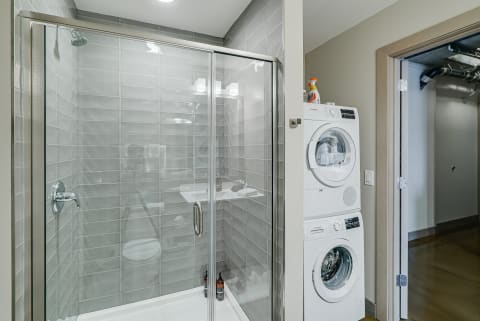 A contemporary bathroom with a glass shower enclosure and a stacked washer and dryer unit.