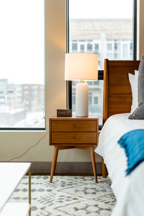 Modern bedroom with a wooden nightstand, lamp, and digital clock beside a bed.