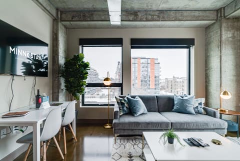 Modern living room with grey sofa, white table, and large windows overlooking cityscape.