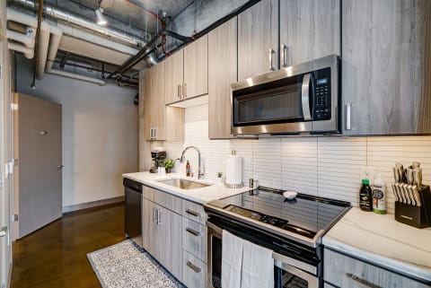 A contemporary kitchen featuring wood cabinetry, stainless steel appliances, and a white countertop.