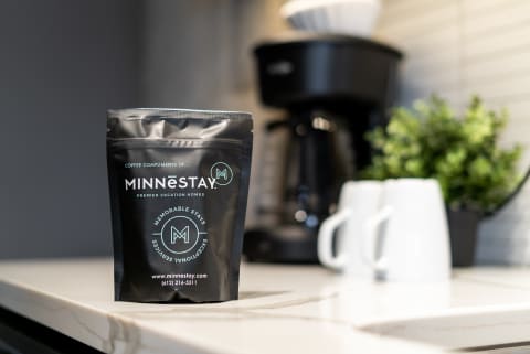 Coffee bag from MINNēSTAY on a kitchen countertop with coffee maker and cups in the background.