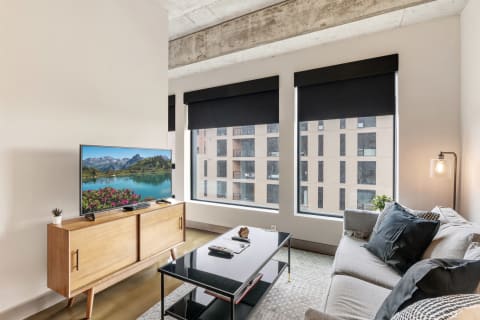 Contemporary living room with a large TV and a cozy sofa, equipped with large windows and modern decor.