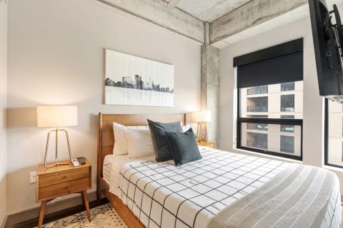 A modern bedroom with a grid-patterned duvet, city skyline art, and a sleek lamp.