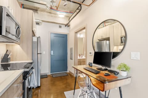 Interior view of a modern studio apartment with kitchen, workspace, and blue front door.