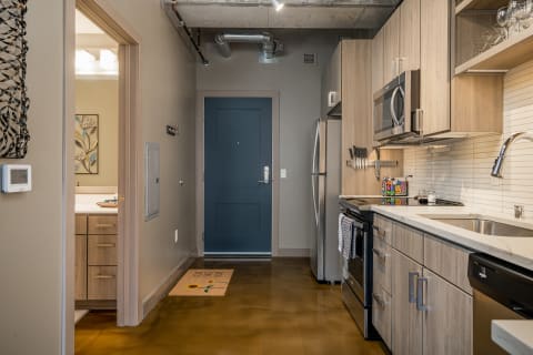 A neatly organized kitchen and entryway in an apartment, featuring soft beige walls and modern appliances.