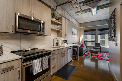 Contemporary kitchen featuring stainless steel appliances connected to a living space with a gray sofa and colorful accents.