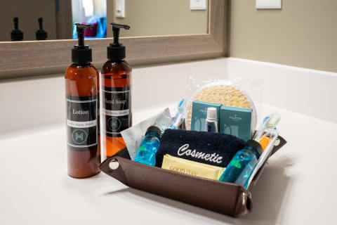 Bathroom counter displaying lotion, hand soap, and assorted toiletries in a brown tray.