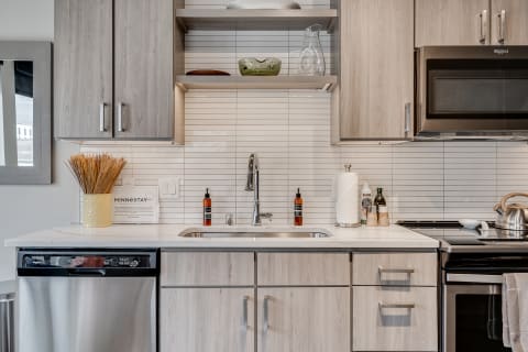 A contemporary kitchen with light wood cabinetry, a sink, and various kitchen items on the counter.