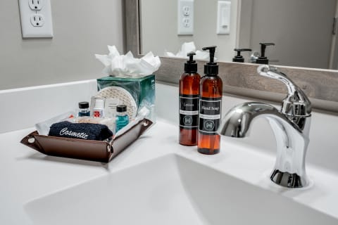 A neatly arranged bathroom counter with lotion, hand soap, and a selection of toiletries in a brown tray.