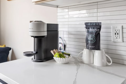 A stylish coffee station with a Nespresso machine, ceramic bowl with tea bags, and white coffee mugs.