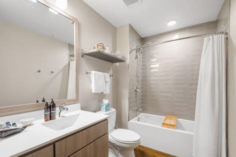 A modern bathroom with a bathtub, shower, and sink, featuring decorative items and a light wood vanity.