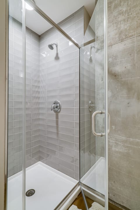Modern shower with glass door and light gray tiled walls.