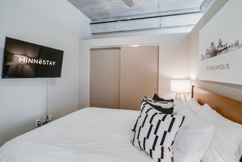 Stylish hotel room with a bed, patterned pillows, a flat-screen TV, and minimalist decor.