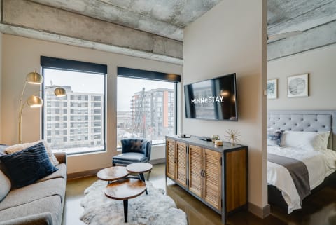 Stylish studio apartment featuring a cozy sofa, accent chair, and a sleek bed area.